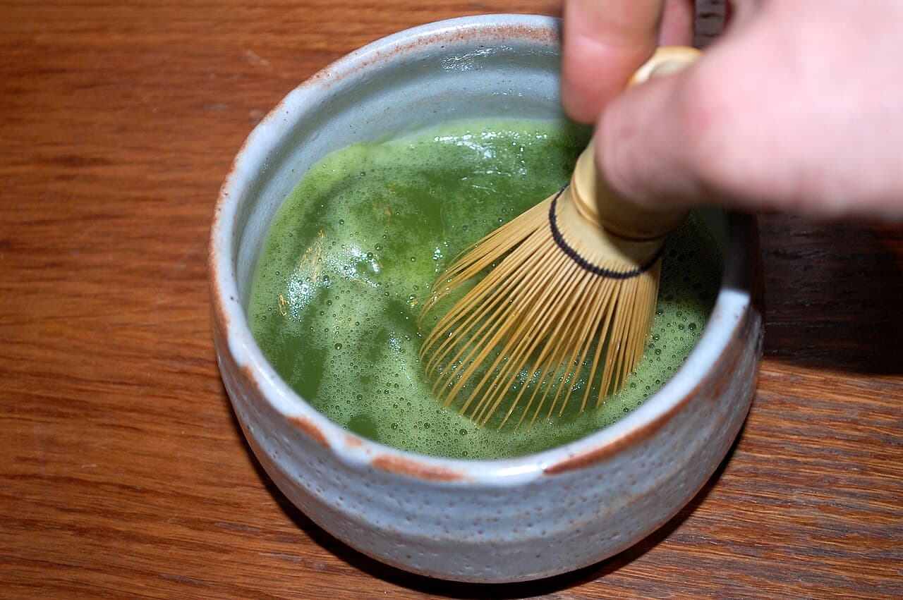 Whisking matcha with a bamboo chasen in a tea bowl to build foam